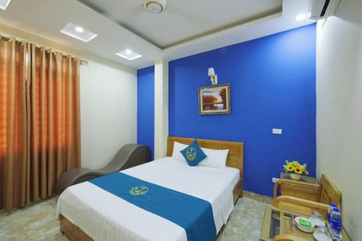 A hotel room with a bed, a desk, a chair, a window with curtains, and a wall with a picture.