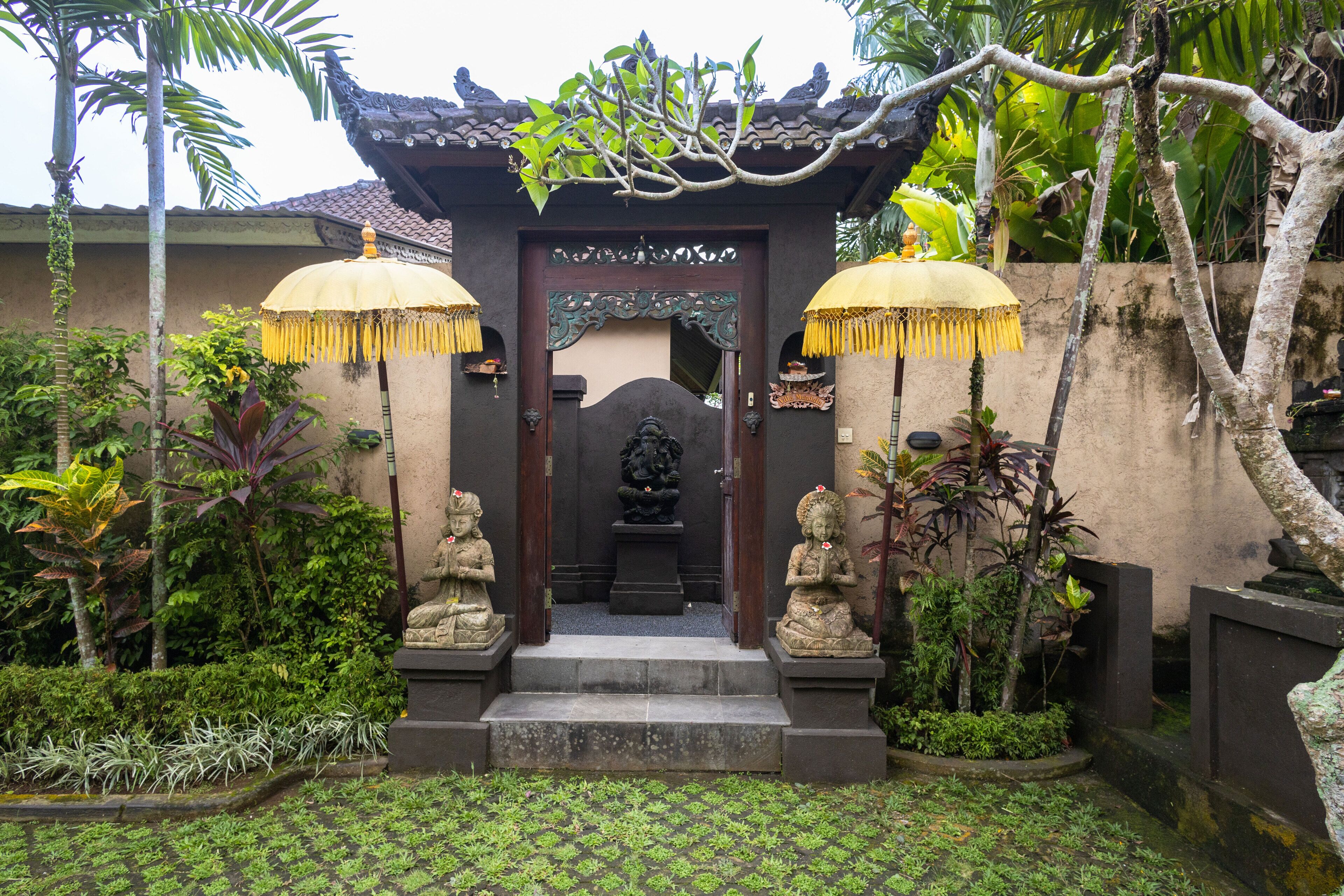 A traditional gate with two statues, a tiled pathway, and lush greenery.