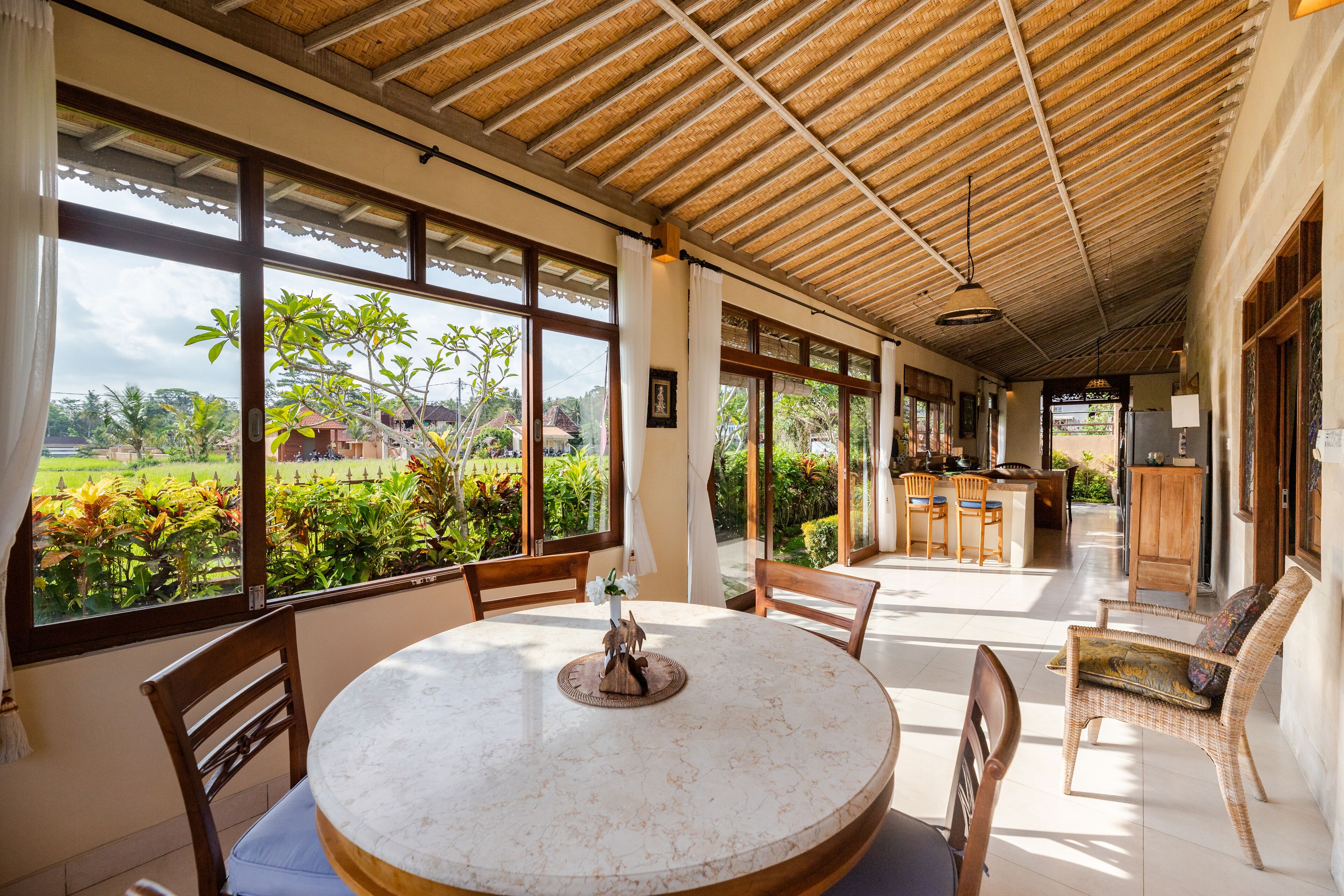 A spacious dining area with a round table, chairs, and a view of a lush garden through large windows.