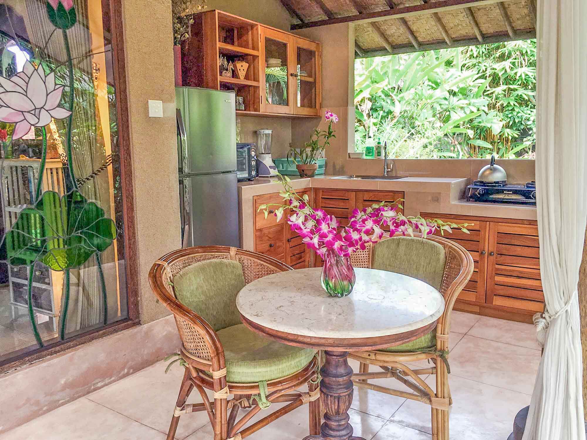Una cocina con mesa, sillas, refrigerador, alacenas y ventana con vista a zonas verdes.