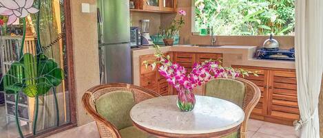 A kitchen with a dining table, chairs, a refrigerator, cabinets, and a window with a view of greenery.