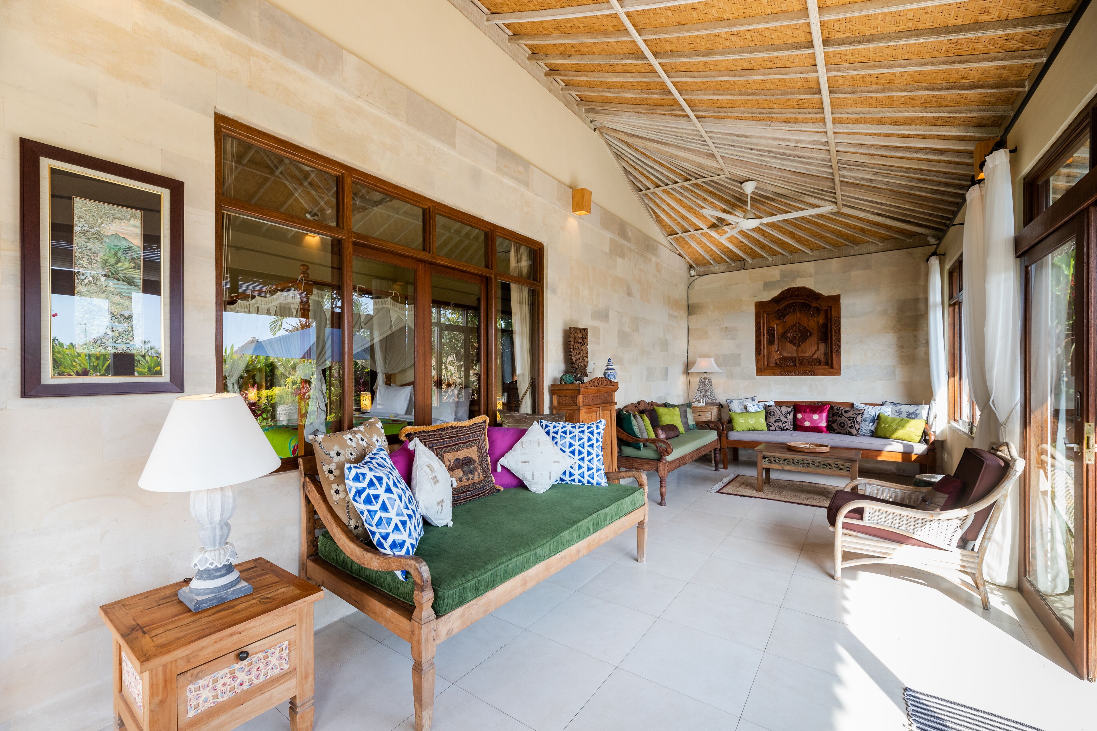 A spacious living area with a wooden bench, a sofa with colorful cushions, and a wooden side table with a lamp.