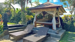 A gazebo with a thatched roof, surrounded by lush greenery and palm trees. - Devi's Place (Ubud)