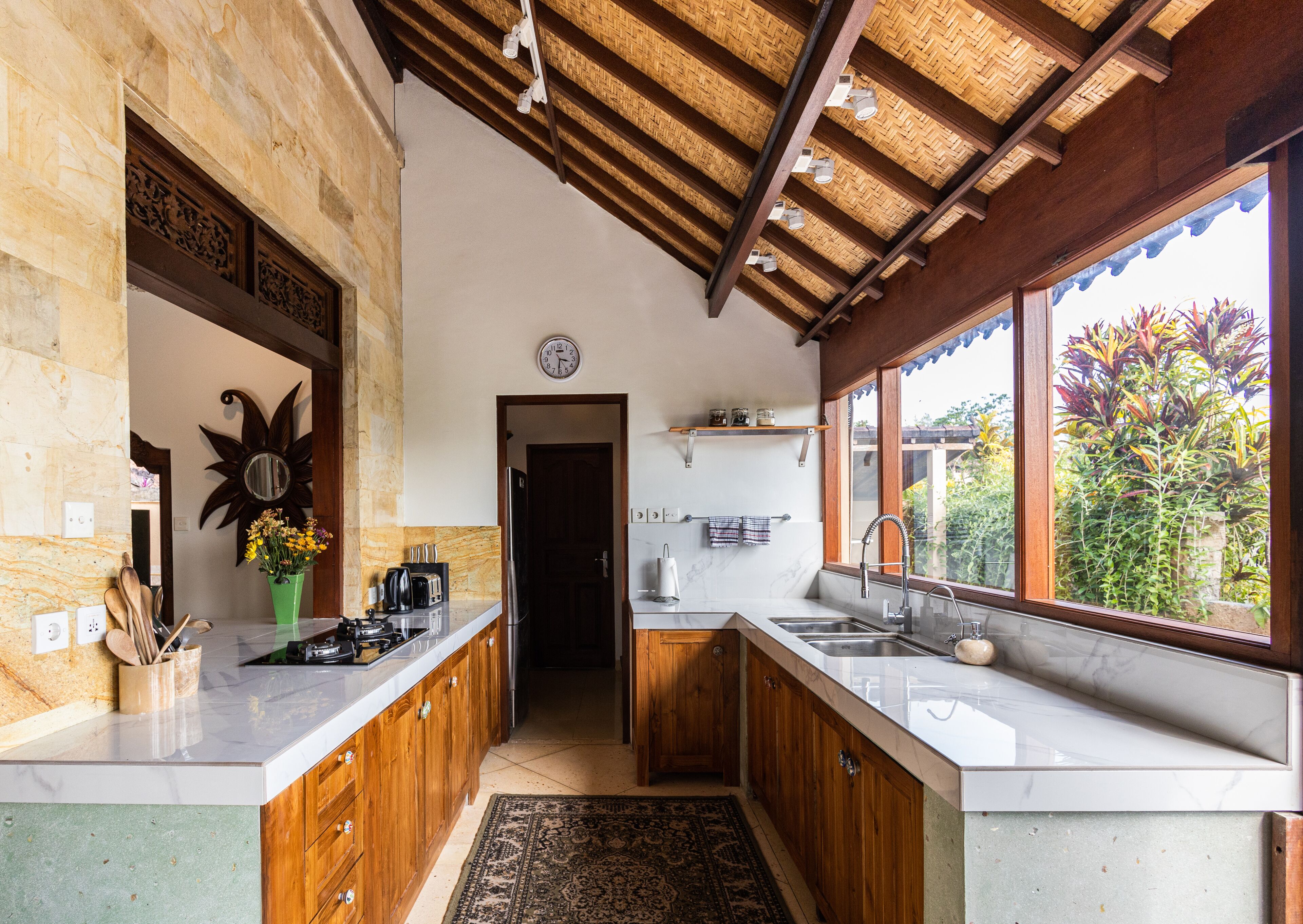 A kitchen with wooden cabinets, a marble countertop, a large window with a view, and a ceiling with a woven pattern.