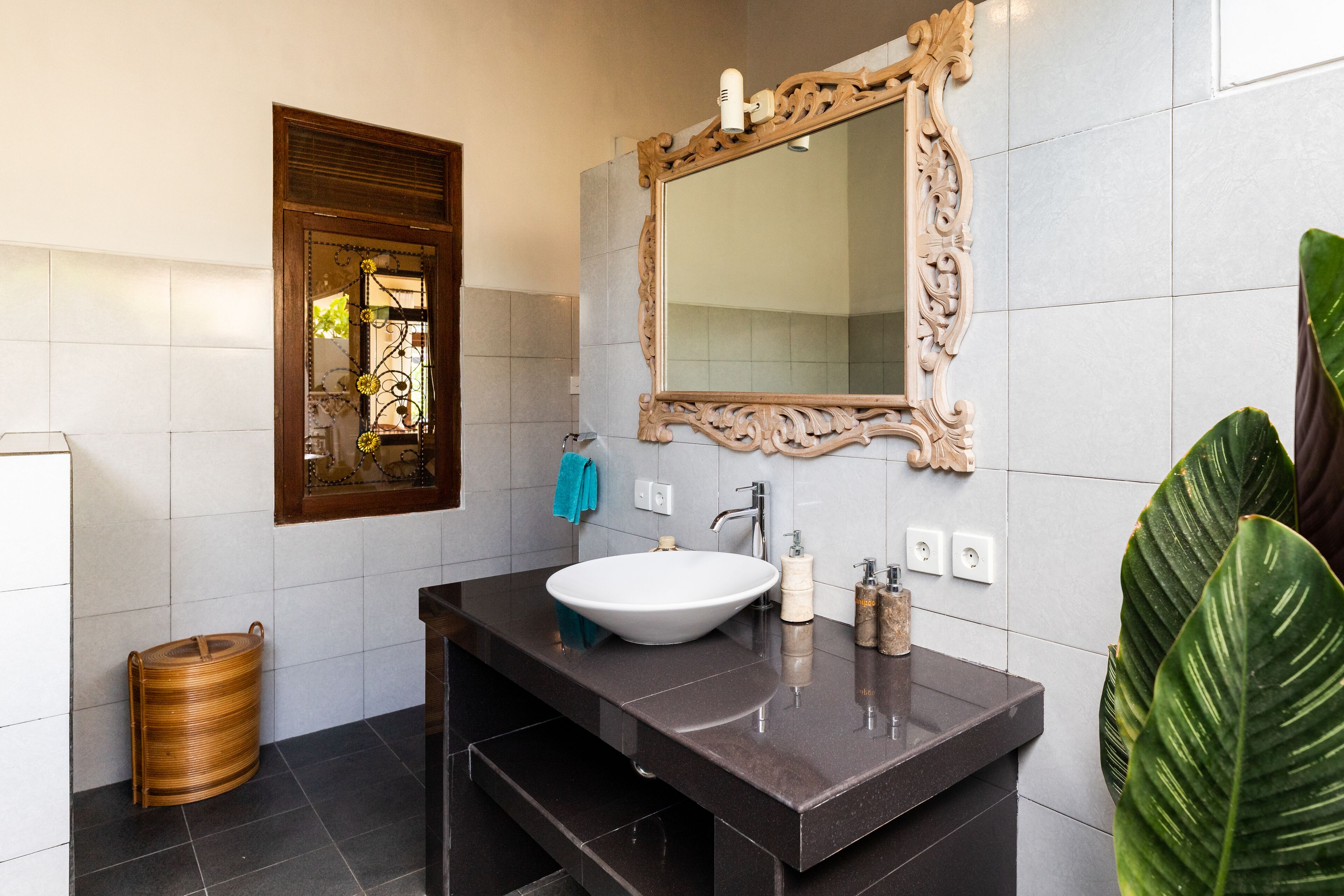A modern bathroom with a large mirror, dark marble countertop, and a white sink.