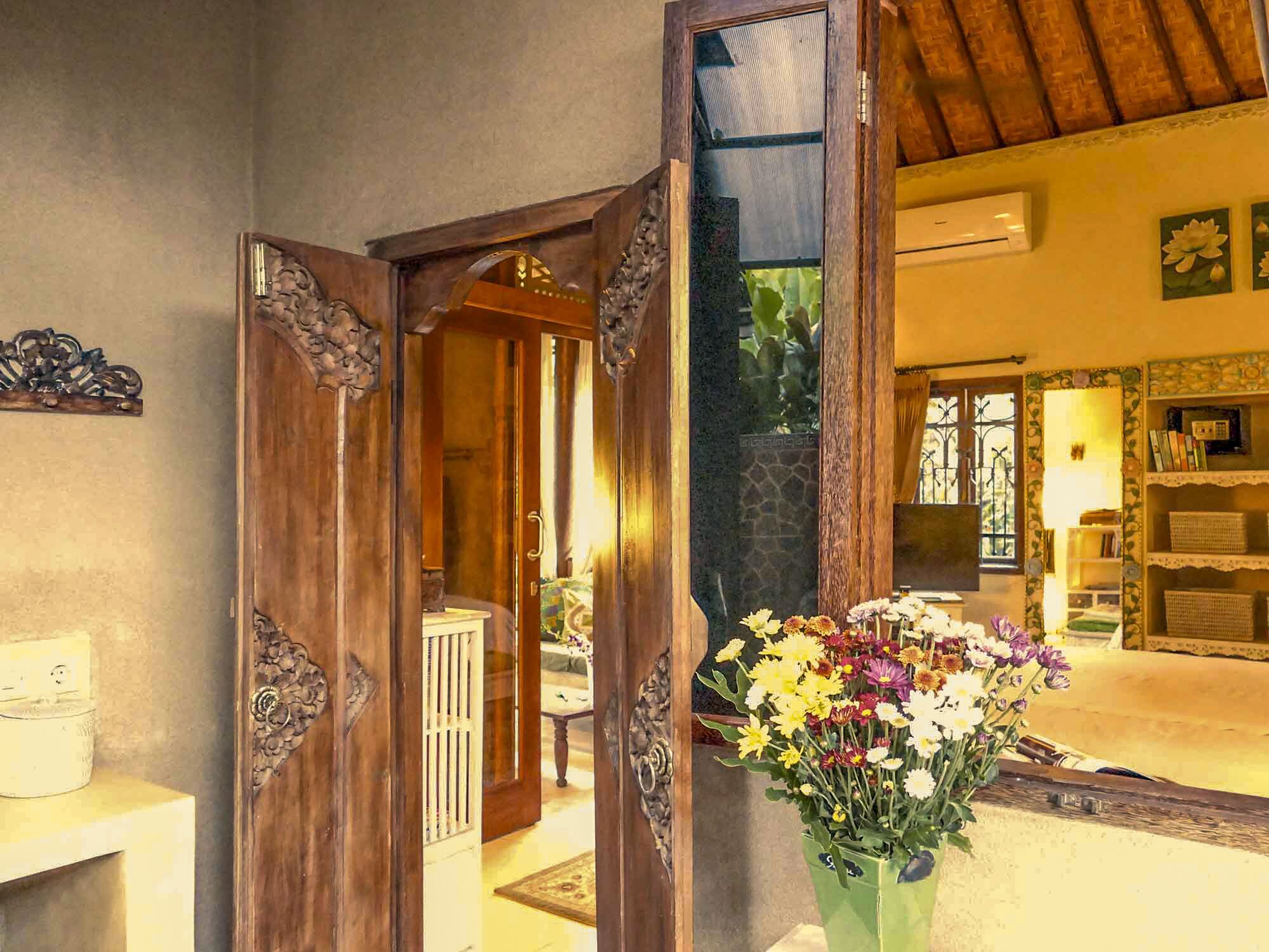 Una porta in legno con decorazioni elaborate, un soggiorno con un divano e un tavolino, e un vaso verde con fiori.