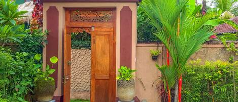 Una puerta de madera con un panel decorativo, flanqueada por plantas en macetas y una pared de piedra.
