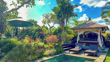 Un área junto a la piscina con sillones de descanso, un pabellón y abundante follaje.