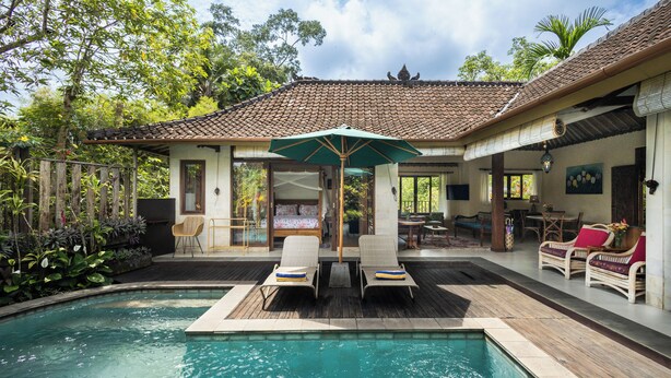 A pool area with lounge chairs, a covered seating area, and a building with a tiled roof. - Devi's Place (Ubud)