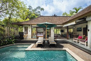 A pool area with lounge chairs, a covered seating area, and a building with a tiled roof. - Devi's Place (Ubud)