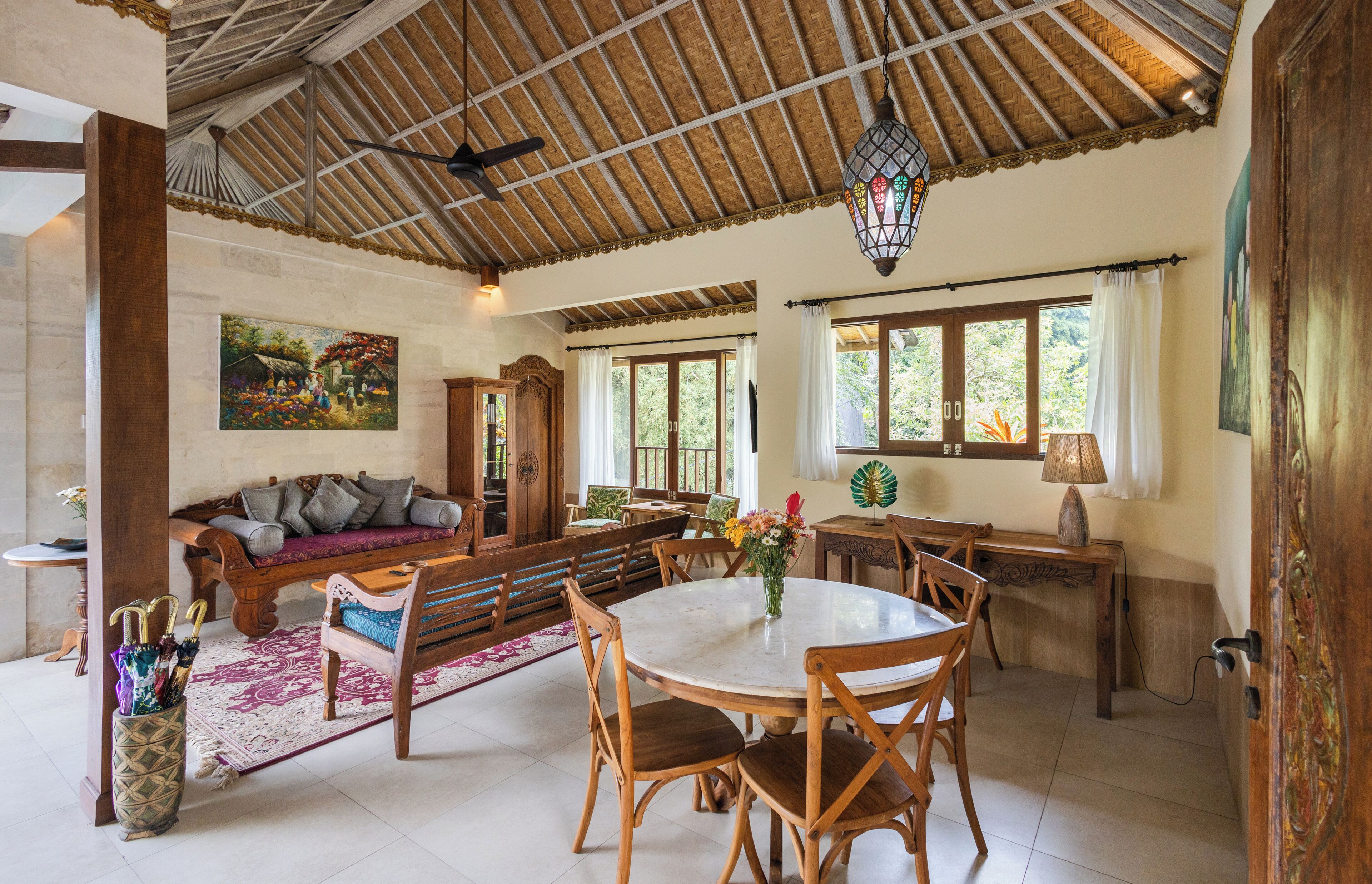 A spacious living area with a wooden ceiling, a sofa, a dining table with chairs, and a painting on the wall.