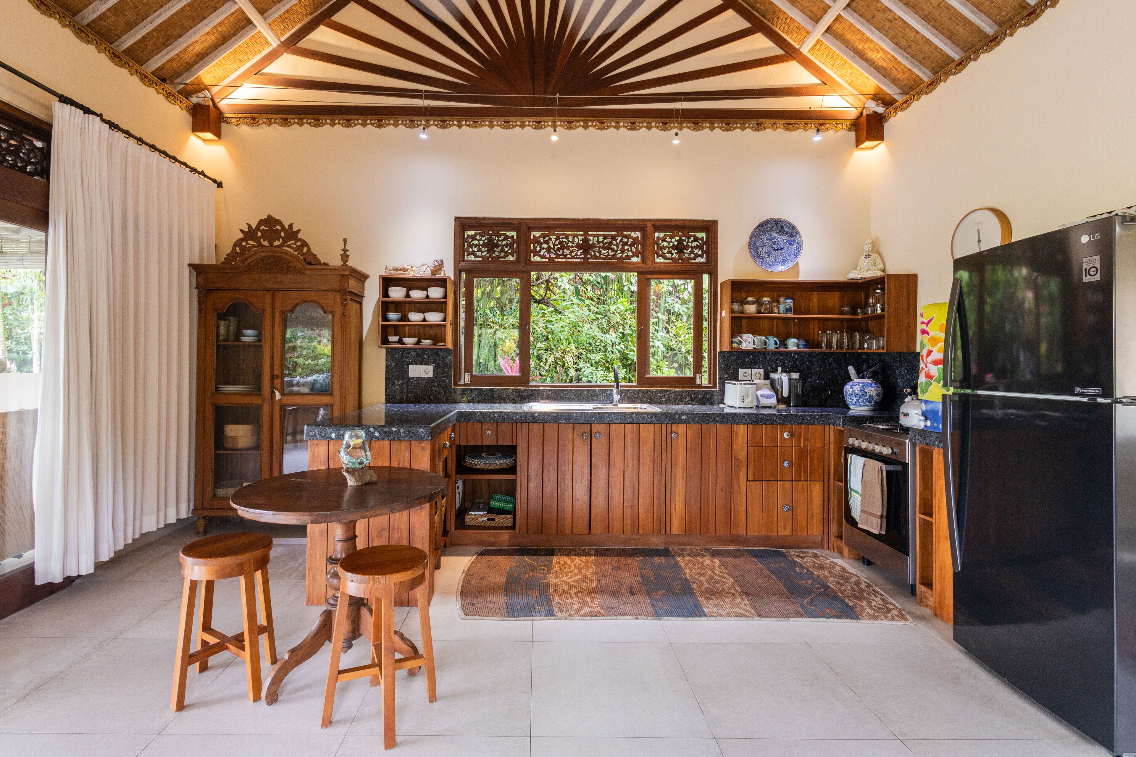 A kitchen with wooden cabinets, a black refrigerator, and a window with a view of greenery.