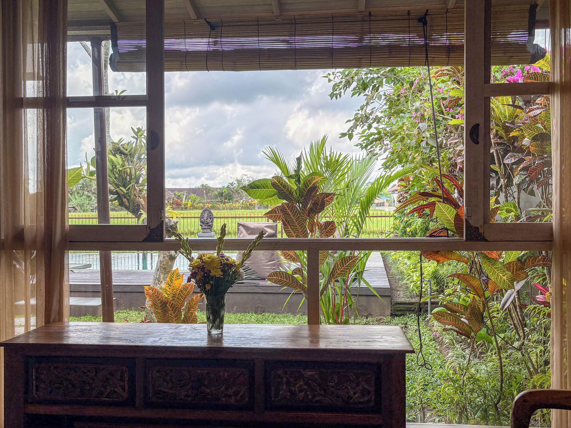 A view through a window with a wooden table and a vase of flowers.