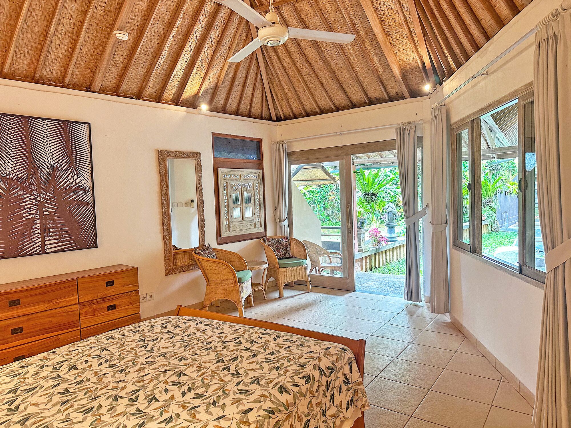 Une chambre à coucher avec un lit, un ventilateur de plafond, une fenêtre et une vue sur le jardin.