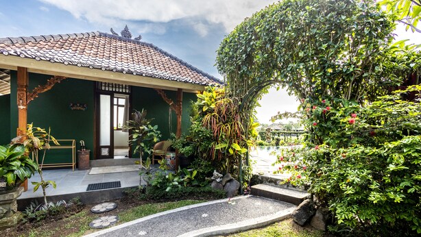 A traditional house with a tiled roof, a wooden porch, and a garden with various plants and a curved pathway.