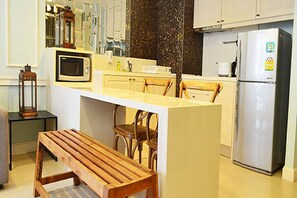 A kitchen with a central island, wooden chairs, a bench, a microwave, a refrigerator, and a dark backsplash. - Marrakesh Residence Hua Hin by Puppap (Hua Hin)