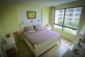 A bedroom with a bed, a nightstand, a window with a view of buildings, and a framed picture on the wall.