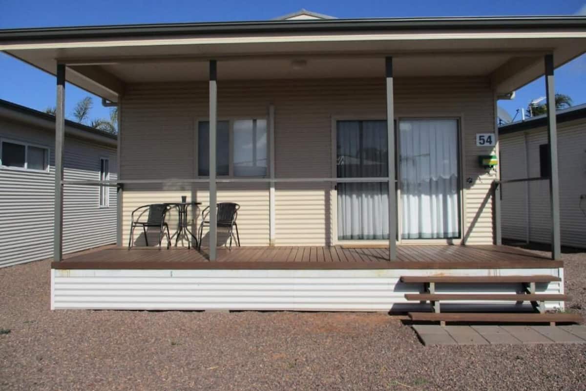Une maison mobile de plain-pied dotée d’un porche couvert, d’un petit espace patio et d’une plaque portant le numéro « 54 ».