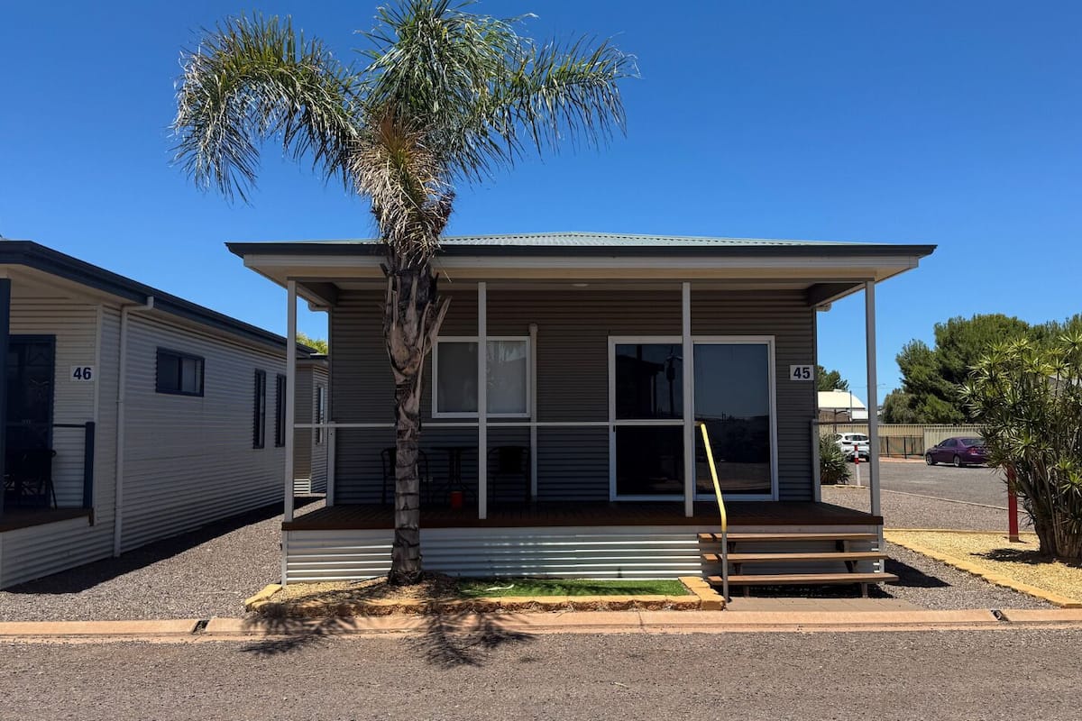 Une maison mobile de plain-pied, dotée d’un porche abrité, d’un palmier devant et surplombée d’un ciel bleu clair.