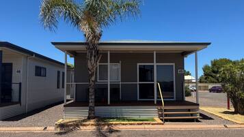 A single-story mobile home with a covered porch, a palm tree in front, and a clear blue sky.