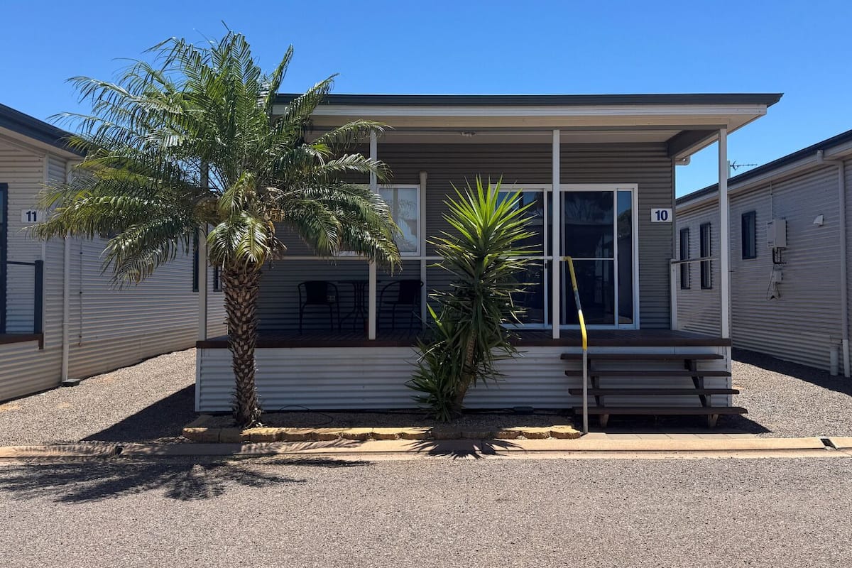 Une maison mobile de plain-pied dotée d’un porche couvert, d’un palmier et d’un petit jardin.