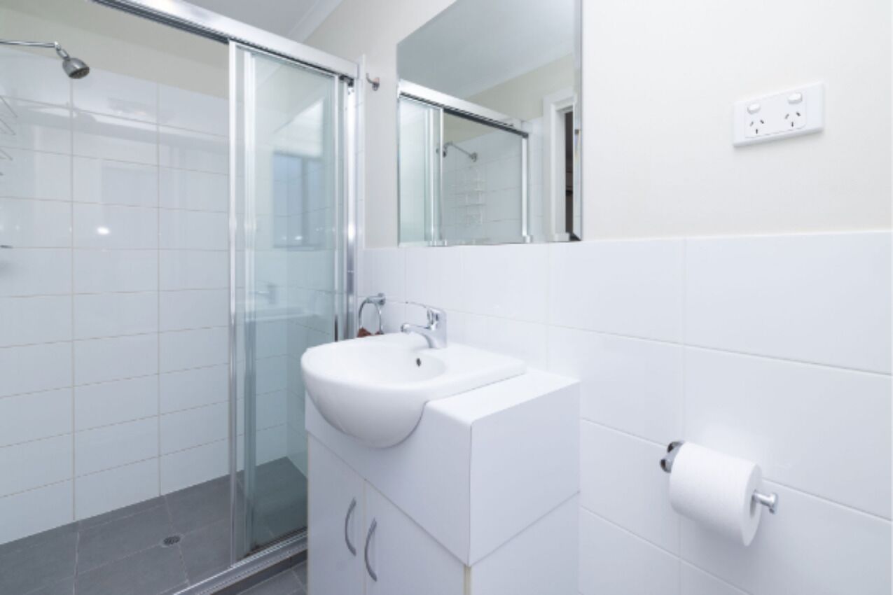 A modern bathroom with a glass shower enclosure, a white sink, and a mirror above it.