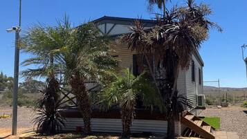 A single-story house with a sloped roof, surrounded by palm trees and a small yard.
