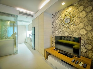 A modern living room with a television on a wooden stand, a wall clock, and a glass door leading to another room.