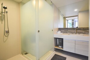 A modern bathroom with a glass shower enclosure, a white vanity with a granite countertop, and a large mirror above the sink. - The Sanctuary Hua Hin by Puppap (Hua Hin)