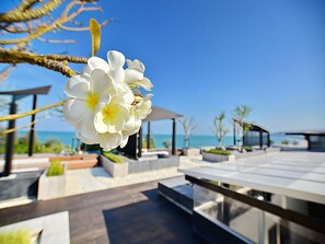 A modern outdoor seating area with a clear view of the ocean, featuring a white flower in the foreground. - The Sanctuary Hua Hin by Puppap (Hua Hin)