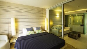 A modern hotel room with a large bed, a sofa, a glass partition, and a small table. - The Sanctuary Hua Hin by Puppap (Hua Hin)
