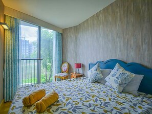 Ein Hotelzimmer mit einem großen Bett, einem Sessel, einem Nachttisch und Blick auf Grün.