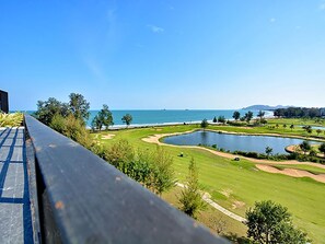 Ein Golfplatz mit Teich, einer Holzterrasse und Blick auf den Ozean.