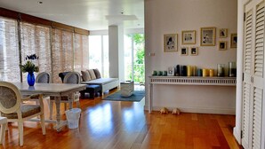A spacious room with a wooden floor, a dining table with chairs, a sofa, and a bookshelf with framed pictures. - Malibu Hua Hin by Puppap (Hua Hin)