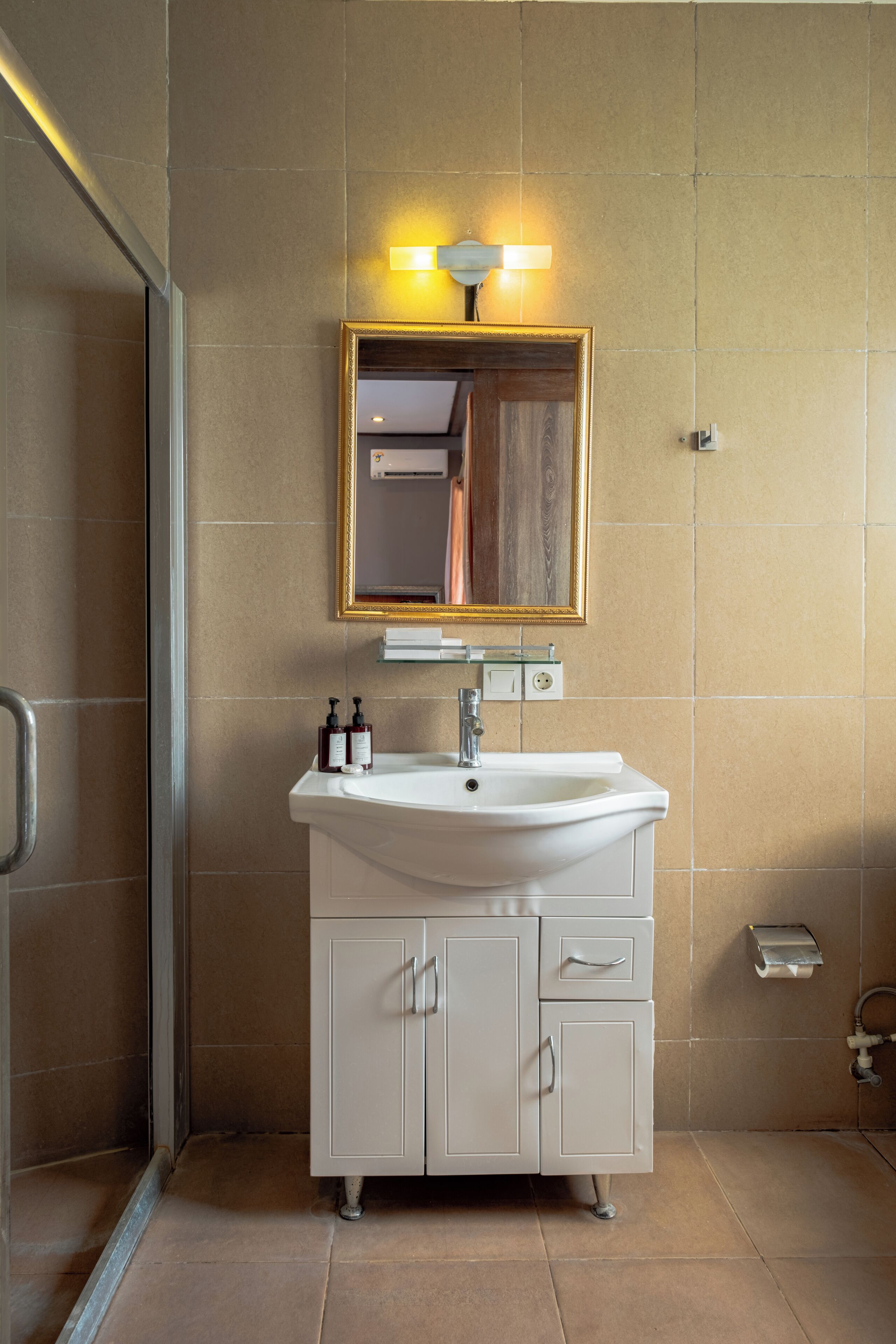 A bathroom with a white sink, a mirror with a gold frame, and a glass shower enclosure.