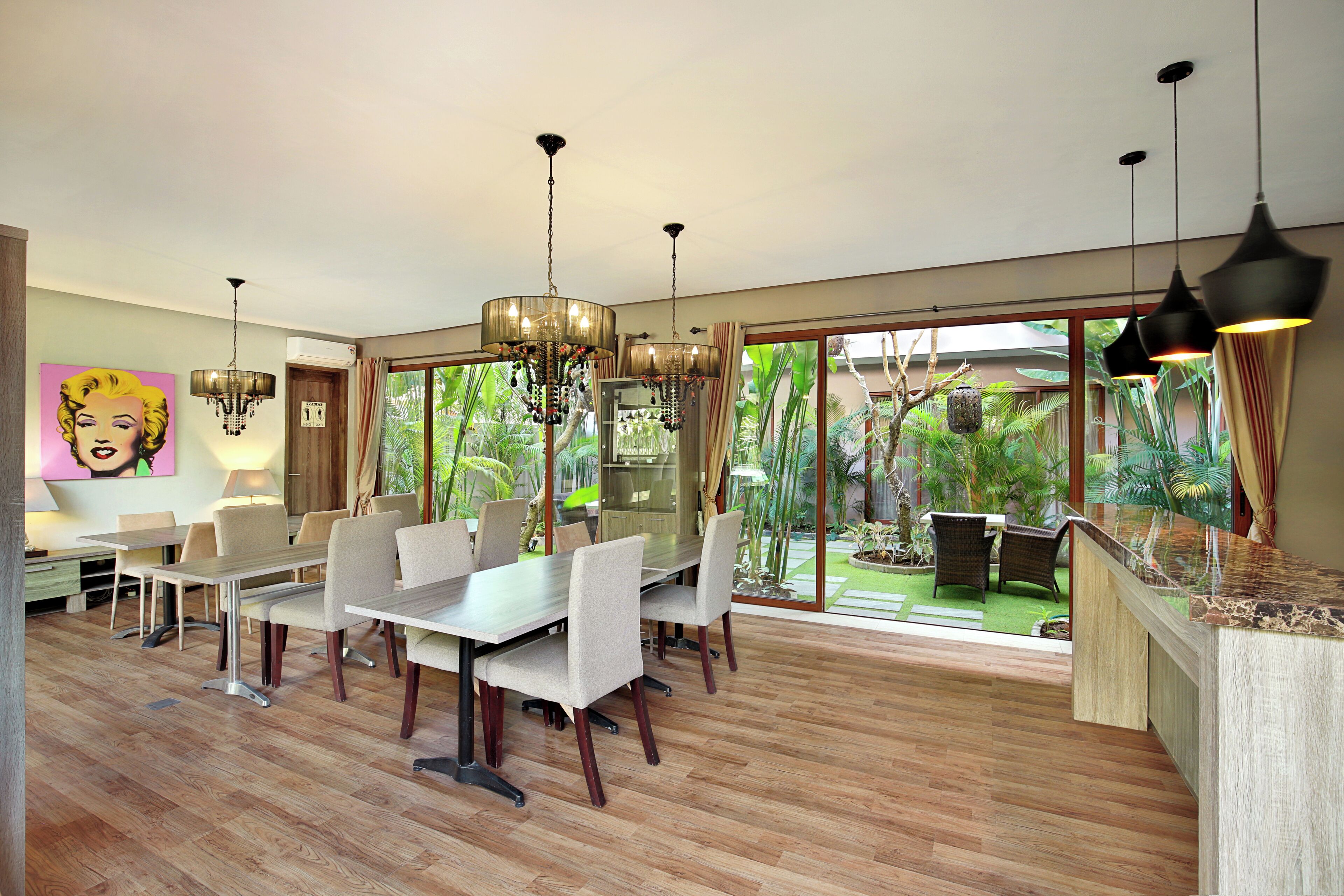 A spacious dining area with a large table and chairs, a chandelier, and a view of a lush garden through large sliding doors.