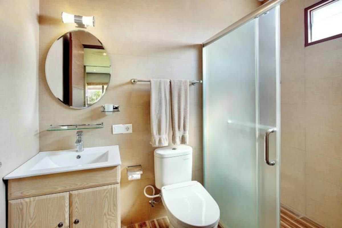 A modern bathroom with a glass shower enclosure, a round mirror, and a wooden vanity.