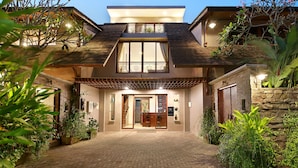 A modern two-story house with a brick entrance, a balcony with a railing, and a stone wall on the right. - Puri Sabina Bed & Breakfast (Jimbaran)