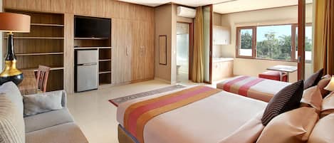 A hotel room with a large bed, a sofa, a TV, a refrigerator, and a window with a view of trees.