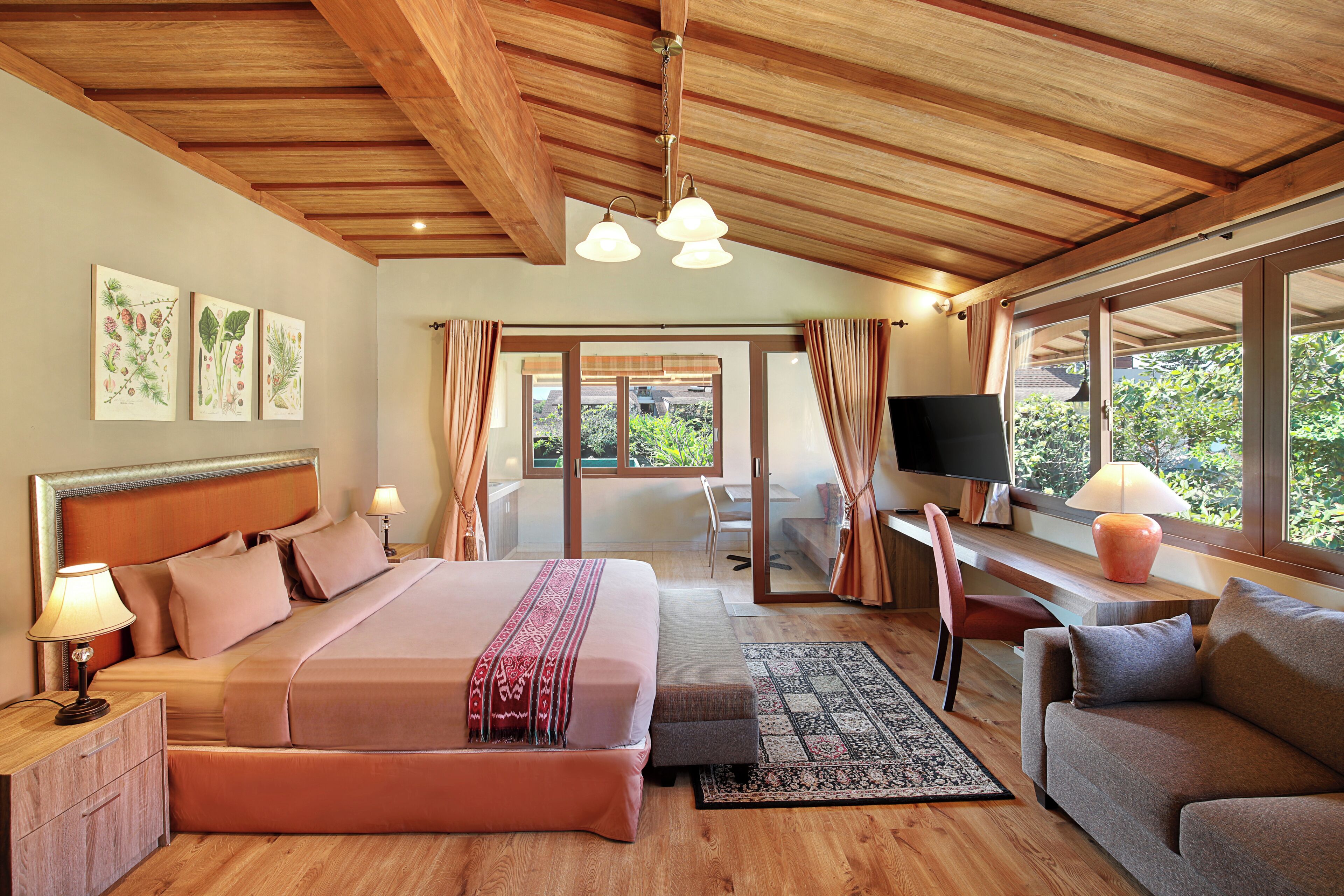 A spacious bedroom with a large bed, a desk with a computer, a TV, and a view of the outdoors.
