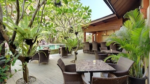 An outdoor patio area with wicker furniture, a pool, and various tropical plants. - Puri Sabina Bed & Breakfast (Jimbaran)