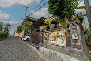 A villa entrance with a stone wall, a gate, and a paved driveway. - Dewi Sri Private Villa (Ubud)