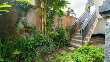 Una escalera de piedra con barandales de metal, rodeada de abundante vegetación y plantas.
