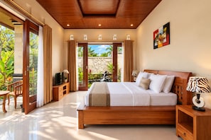 A spacious bedroom with a large bed, wooden headboard, and a view of a tropical garden through a sliding door. - Dewi Sri Private Villa (Ubud)