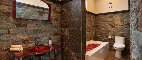 Un baño con pared de piedra, un lavabo rojo, un espejo y un inodoro blanco.
