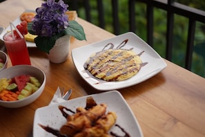 A table with a plate of food, a bowl of fruit, a drink, and a potted plant. - Dewi Sri Private Villa (Ubud)