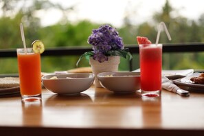 A table with two bowls, a potted plant, and two drinks with straws. - Dewi Sri Private Villa (Ubud)