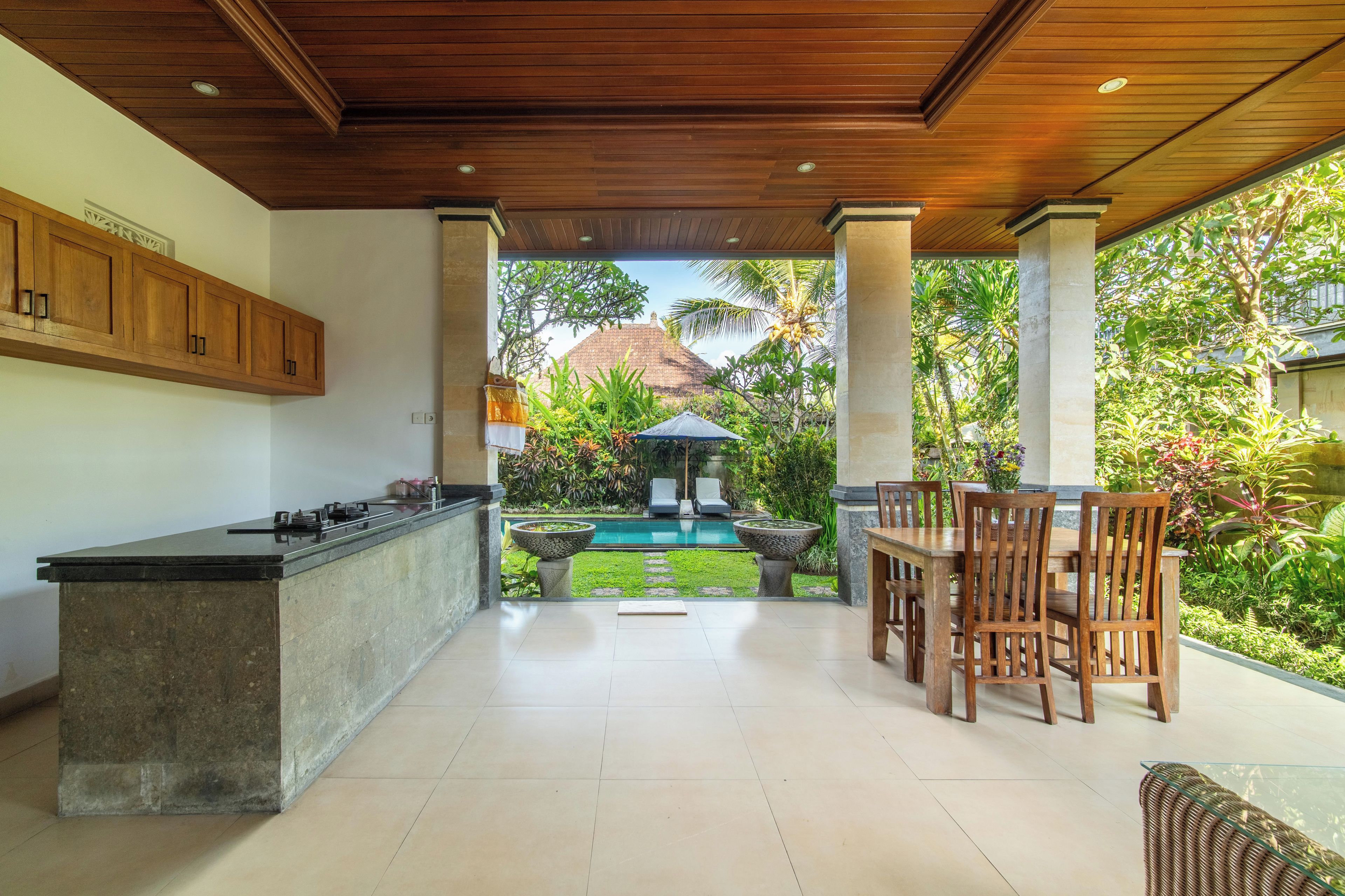 A covered outdoor kitchen area with a pool in the background.