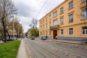 A street with tram tracks, a yellow building with a balcony, and a green tree line. - ASAO Apartments Walking Center Zone (Lviv)
