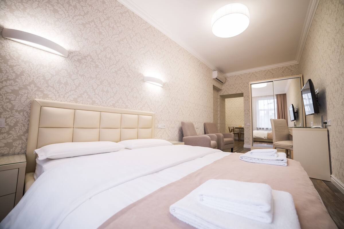 Quarto de hotel com uma cama grande, uma cadeira, uma escrivaninha e uma televisão.